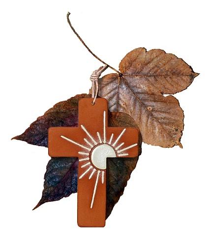 Ein Tonkreuz mit weißem Sonnensymbol als Anhänger vor dekorativen Laubblättern