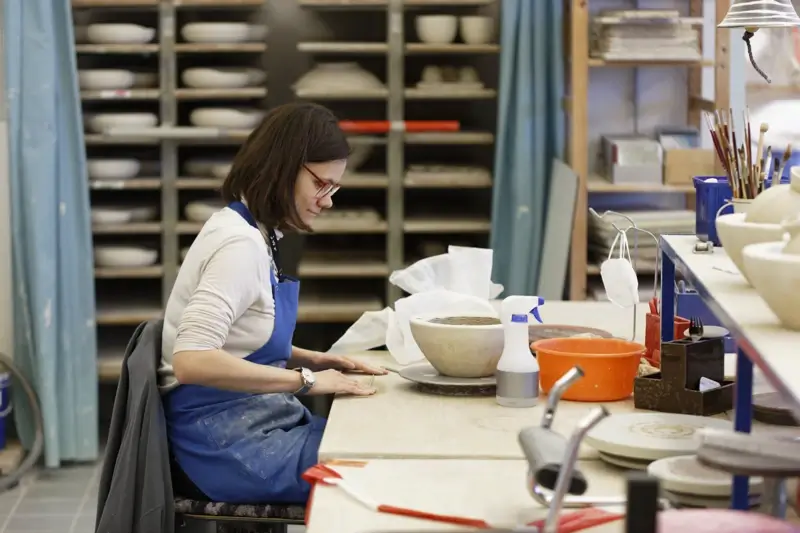 Sitzende Frau vor einem Tisch in einer Werkstatt, die eine Schale töpfert