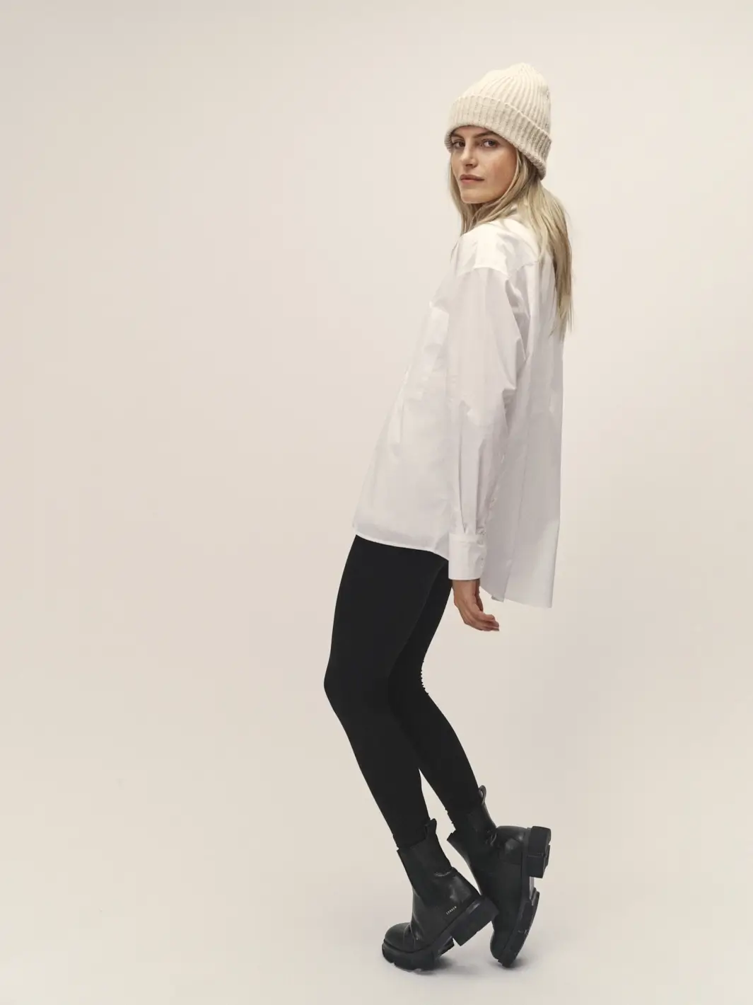 Weibliches Model welches sich nach hinten lehnt, weiße Strickmütze, weißes Oversized Hemd