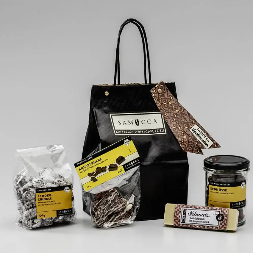 Alle Produkte, die im Geschenkkorb enthalten sind, mit schwarzer Samocca Tüte im Hintergrund