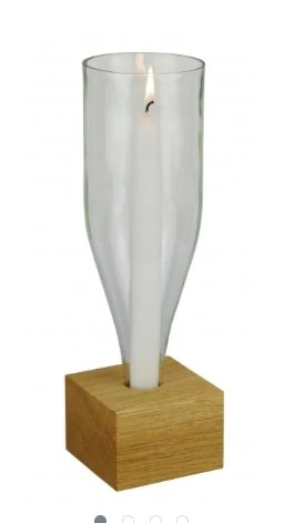 Eine umgedrehte transparente Glasflasche mit offenen Boden, mit brennender Kerze darin auf einem Holzsockel